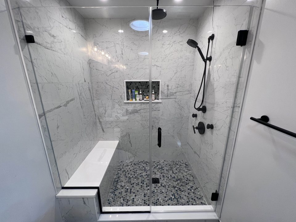 The same alcove after: a frameless glass door and fixed panel with matte black hinges and pull across the opening