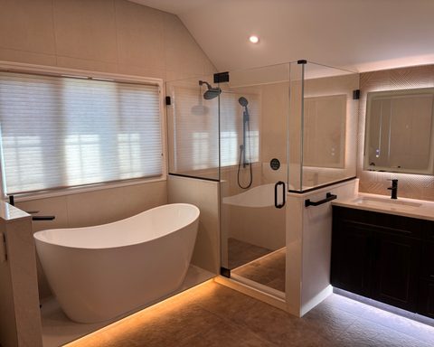 The same bathroom after: a frameless glass enclosure with matte black hardware on the knee walls