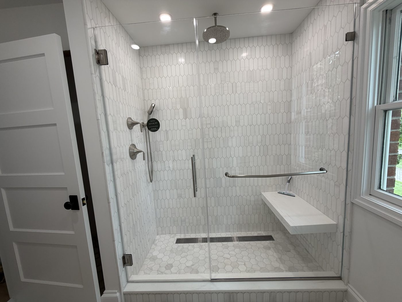 Frameless door and panel on elongated hex tile with a floating bench and chrome hardware
