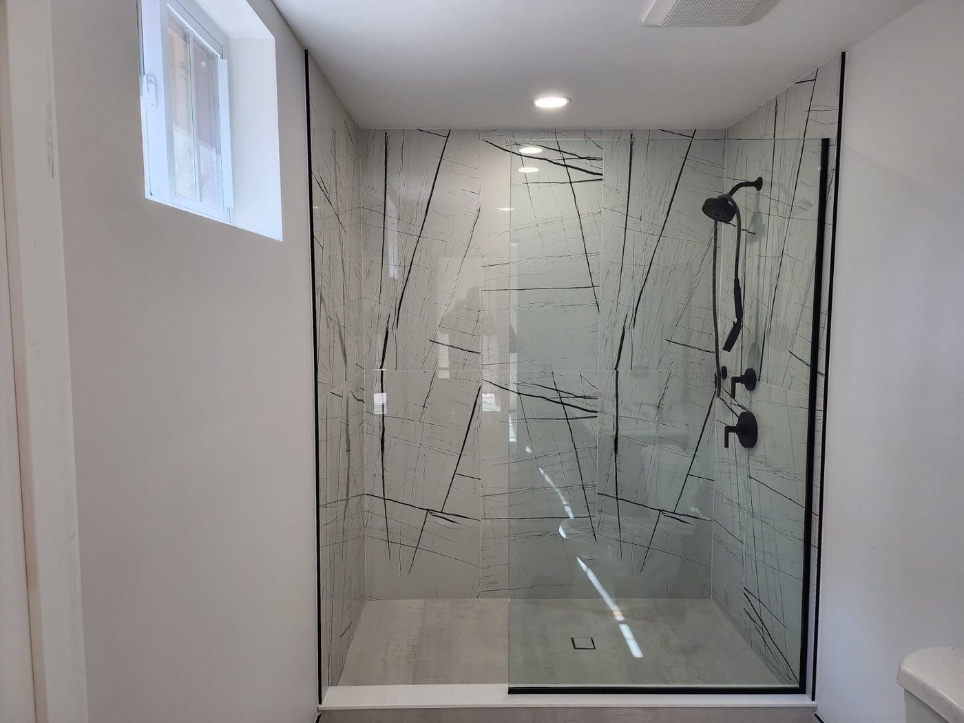 Walk-in shower with a black-edged fixed glass panel and patterned marble-look walls