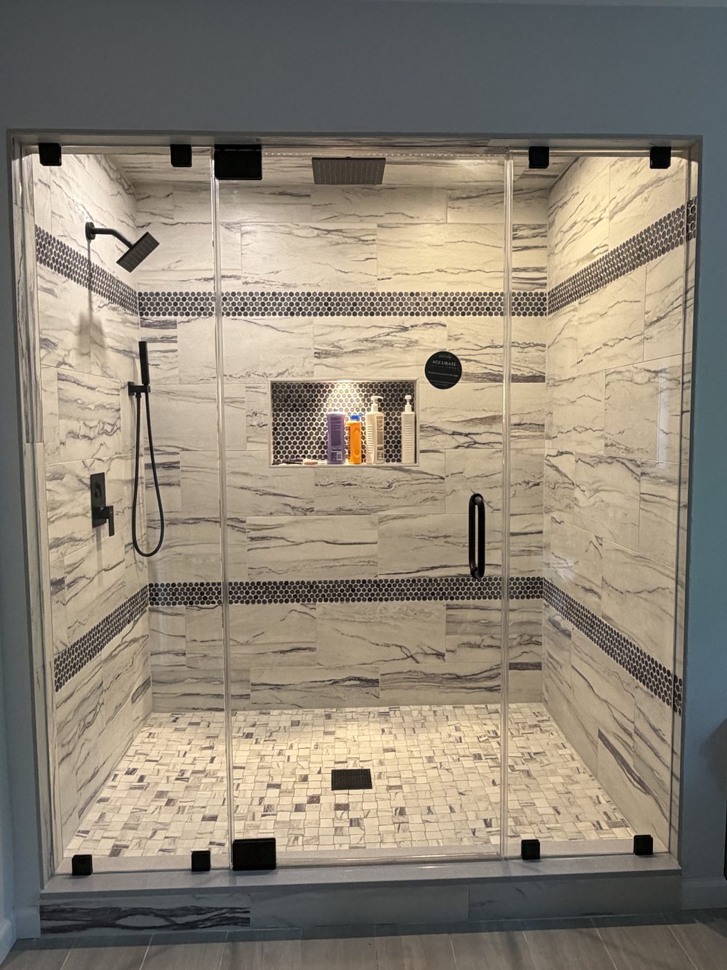 Inline frameless door and panel with matte black hardware, marble tile and penny mosaic bands