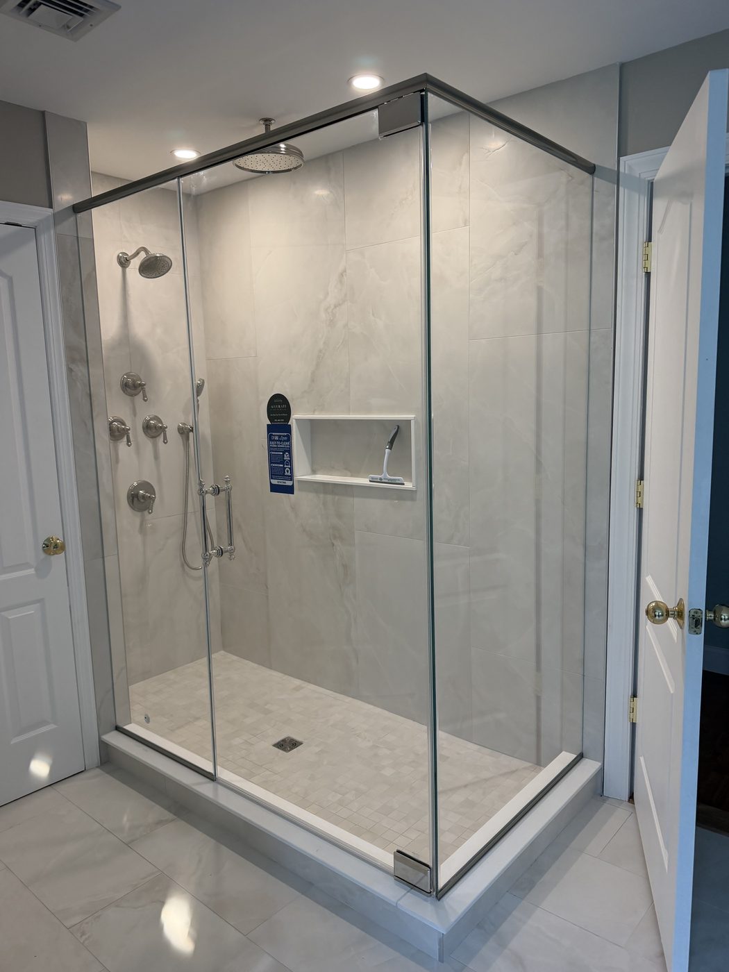 Corner enclosure with a chrome header bar and marble-look tile