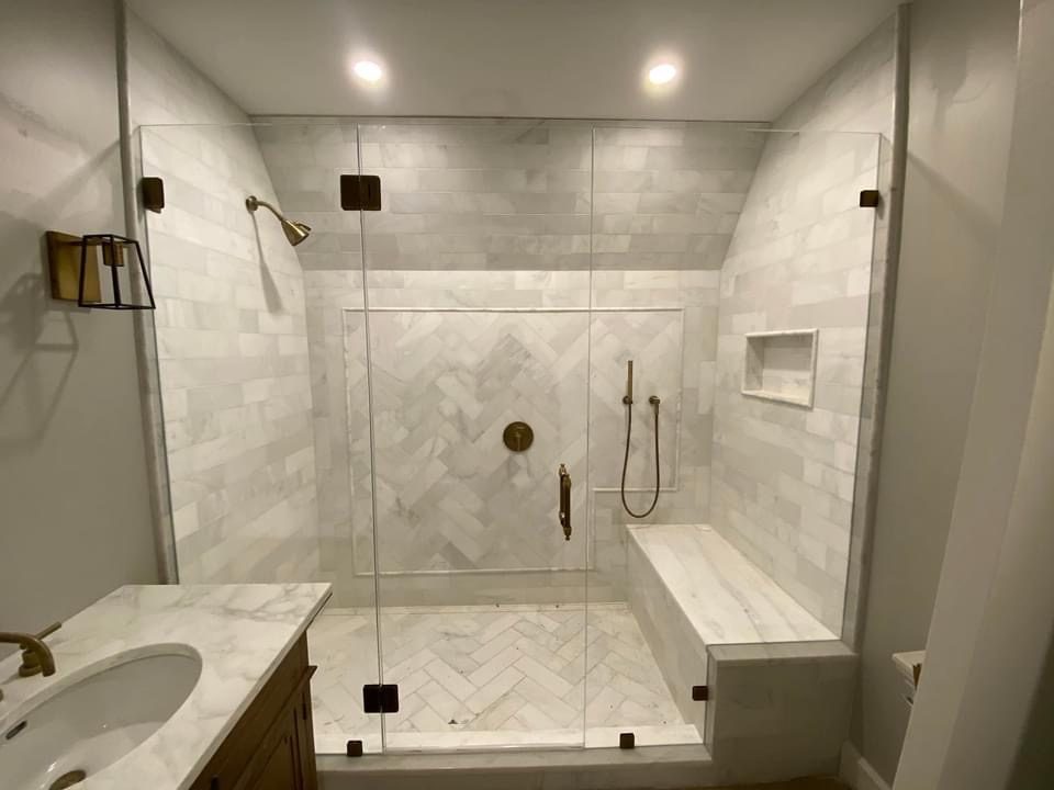 Frameless glass tub enclosure with white marble herringbone tile