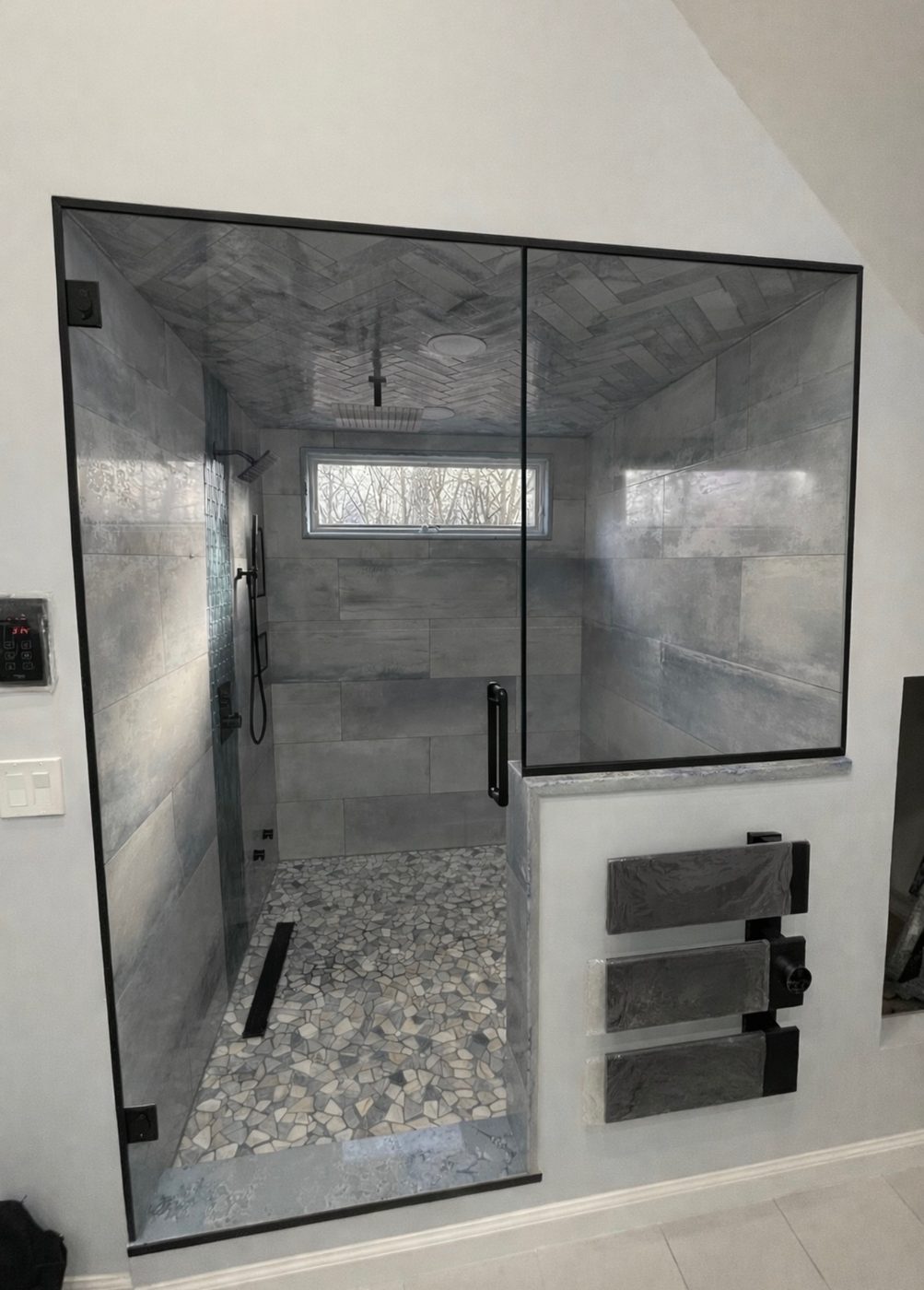 Black-framed glass shower enclosure with gray tile and a pebble-stone floor