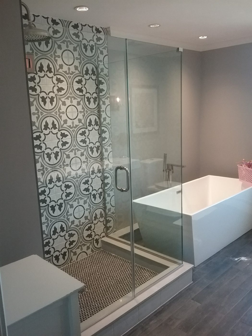 Glass shower beside a freestanding tub with patterned accent wall