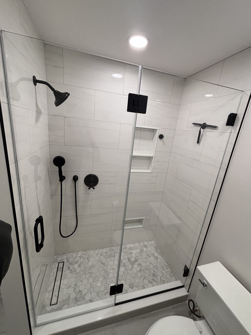 Frameless glass shower with black fixtures and white marble